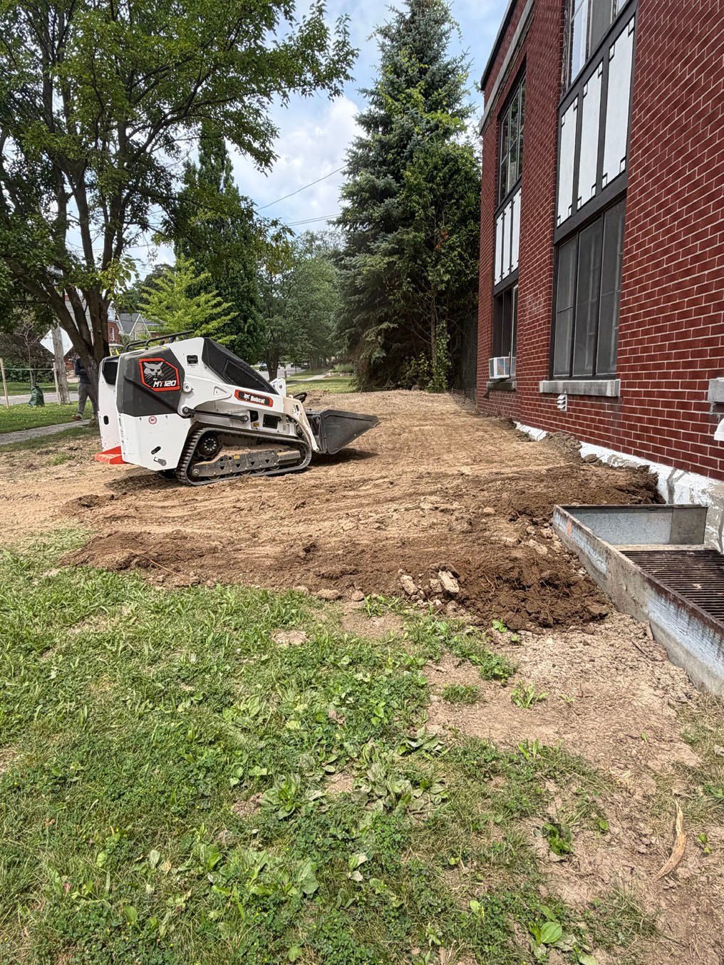 Skid steer stripping and grading the ground beside the brick building in Cherry Hill, Kitchener