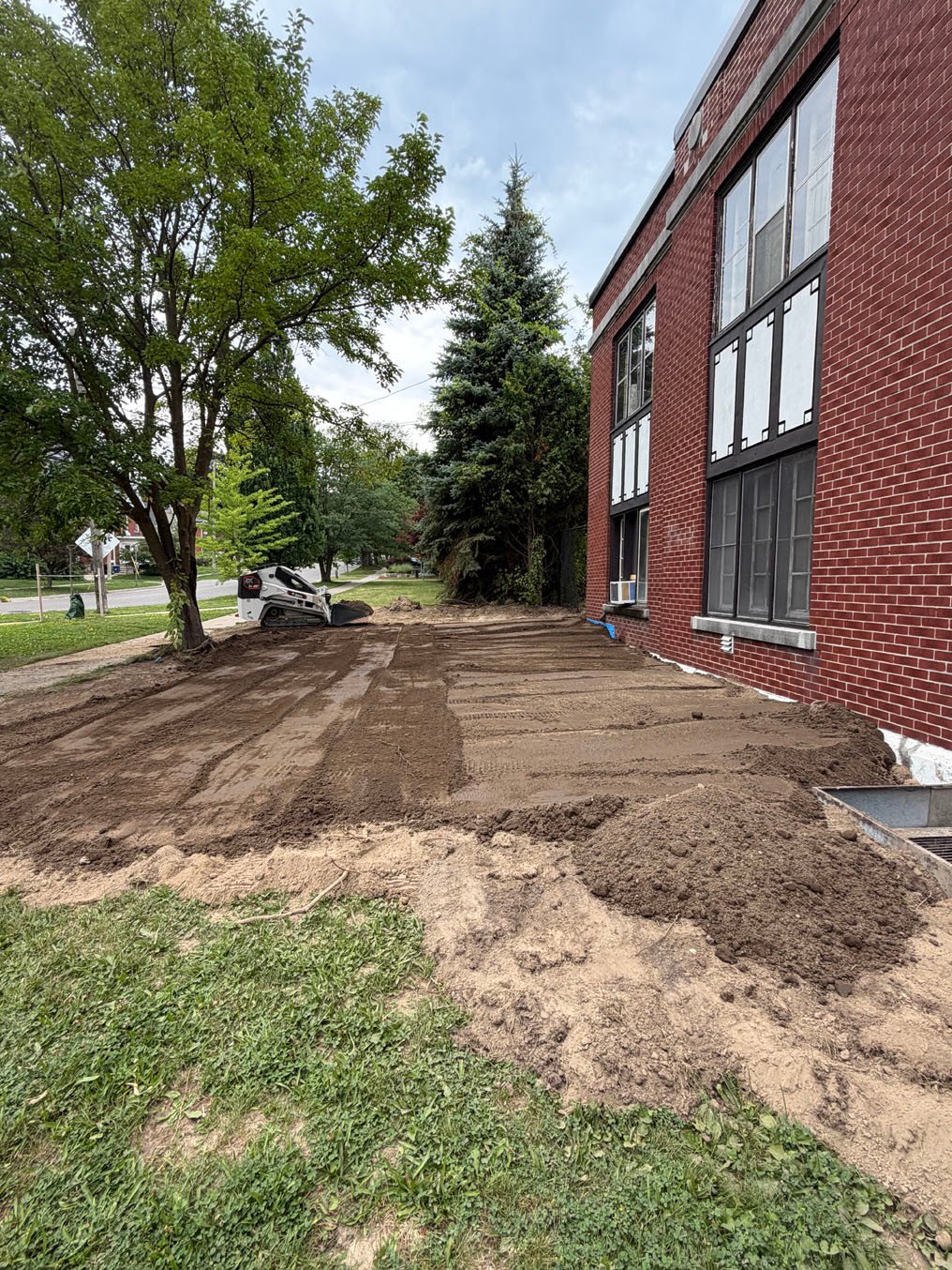 Skid steer spreading fresh topsoil along the building in Cherry Hill, Kitchener