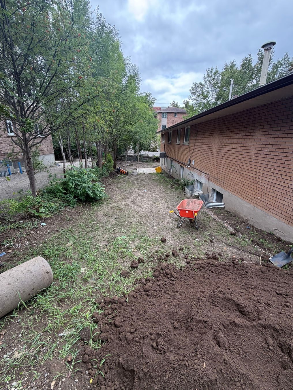 Rough bare ground with soil mounds and debris along the side of a brick two-storey on Columbia Street West, Waterloo