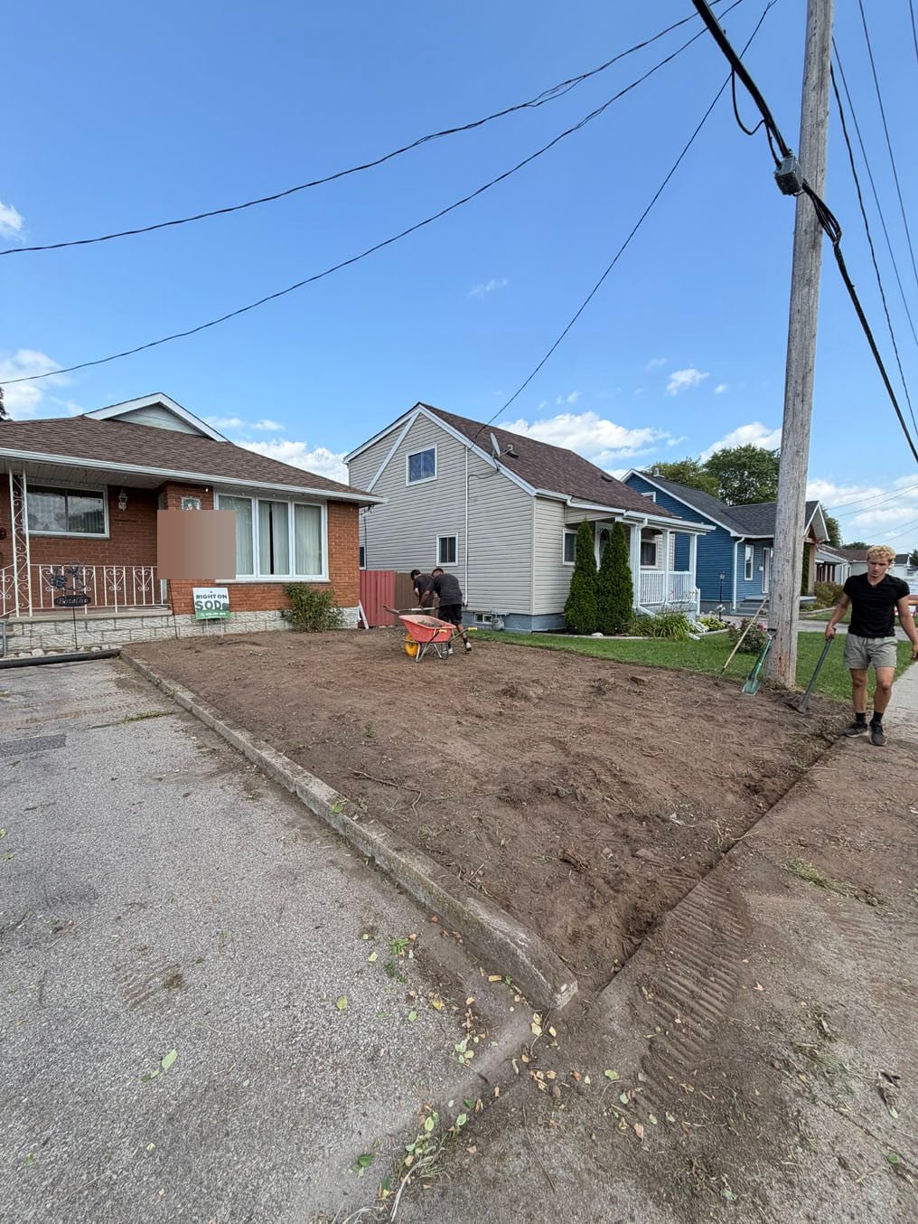 Right On Sod crew raking the cleared front yard level in Galt, Cambridge, the soil graded flush with the driveway curb and the sidewalk