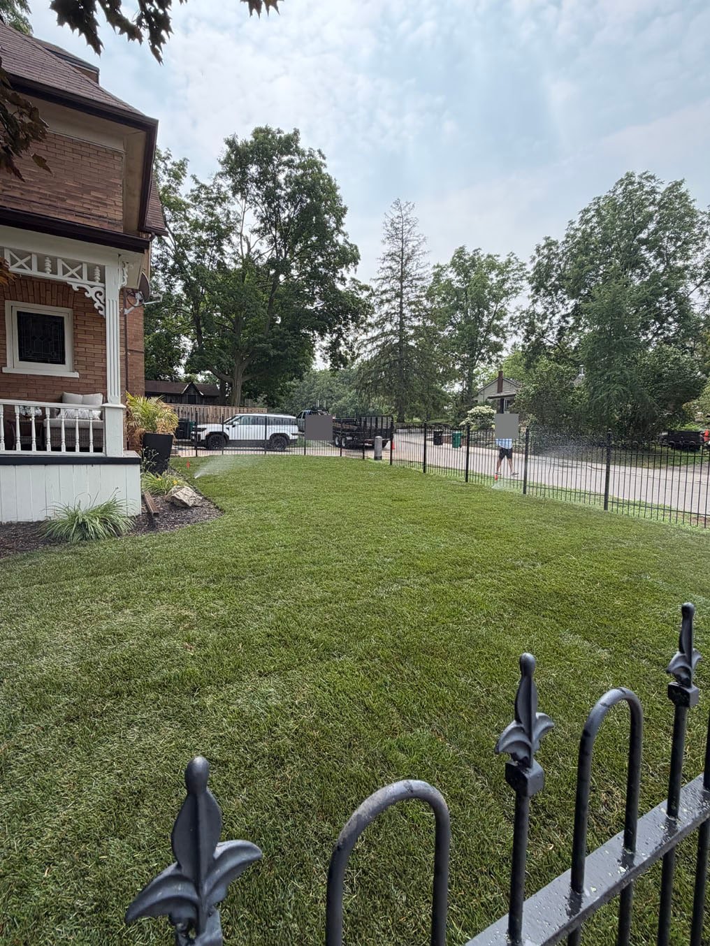 Sprinkler running on the newly laid Kentucky bluegrass lawn inside the iron fence in Hespeler, Cambridge, porch at left