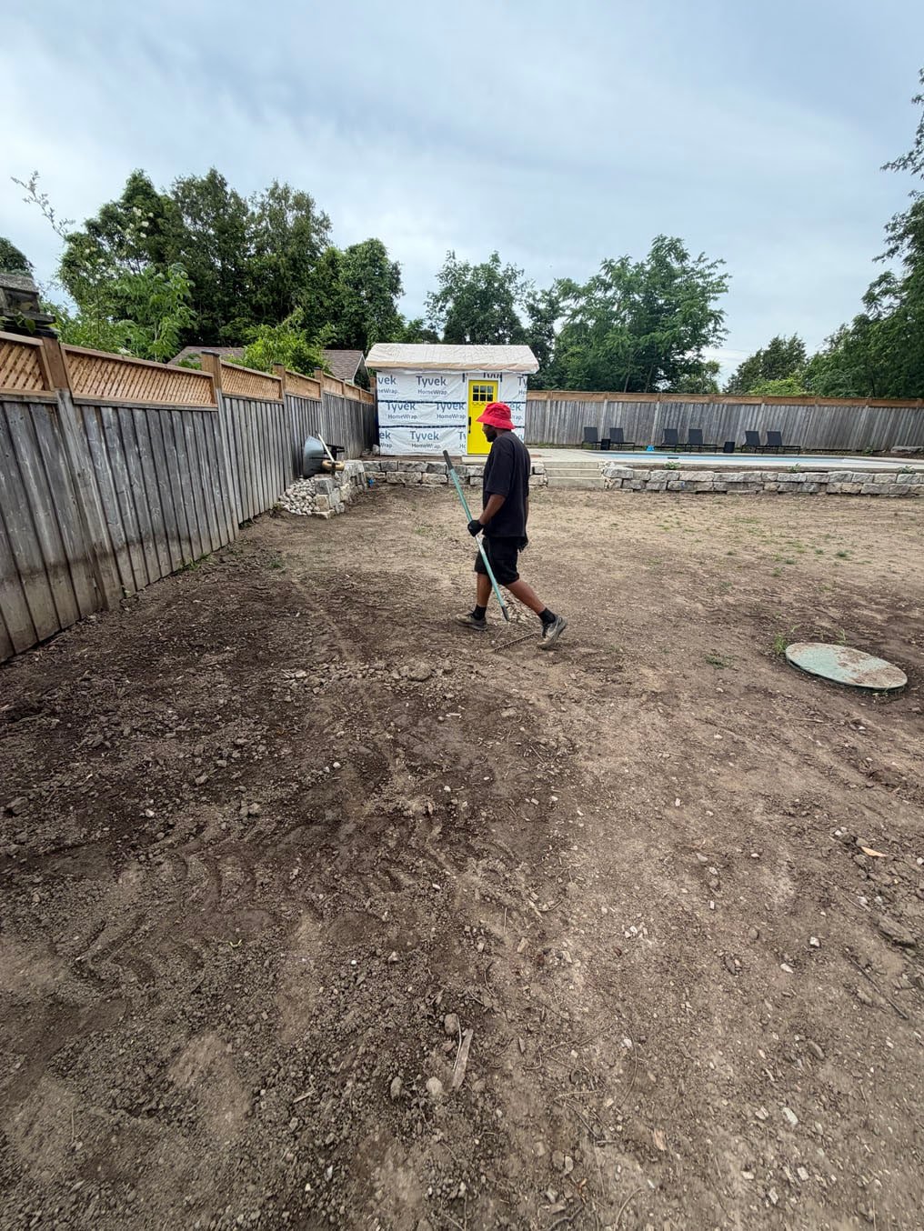 Sod Installation Pioneer Tower West 4 Bare, compacted backyard soil with tyre tracks at a home with a pool in Pioneer Tower West, Kitchener, a crew member raking before topsoil and sod