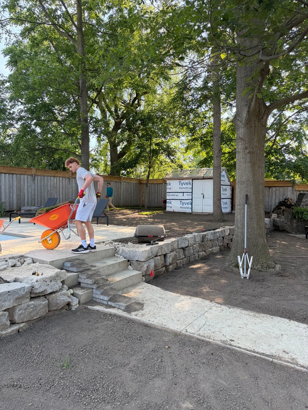 Crew member with a wheelbarrow of Kentucky bluegrass sod rolls at the stone steps between the pool terrace and main yard in Pioneer Tower West, Kitchener