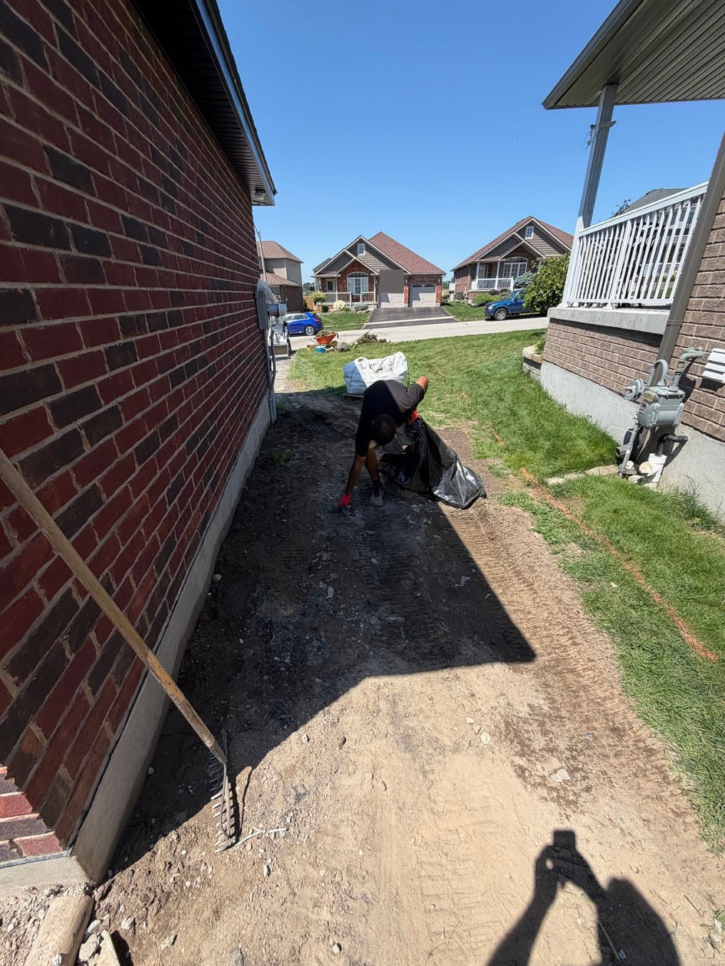 Sod Installation In Plattsville, Ontario 2 Street end of the side yard stripped to bare ground, skid-steer tracks in the dirt, a crew member bagging debris, Plattsville, Ontario