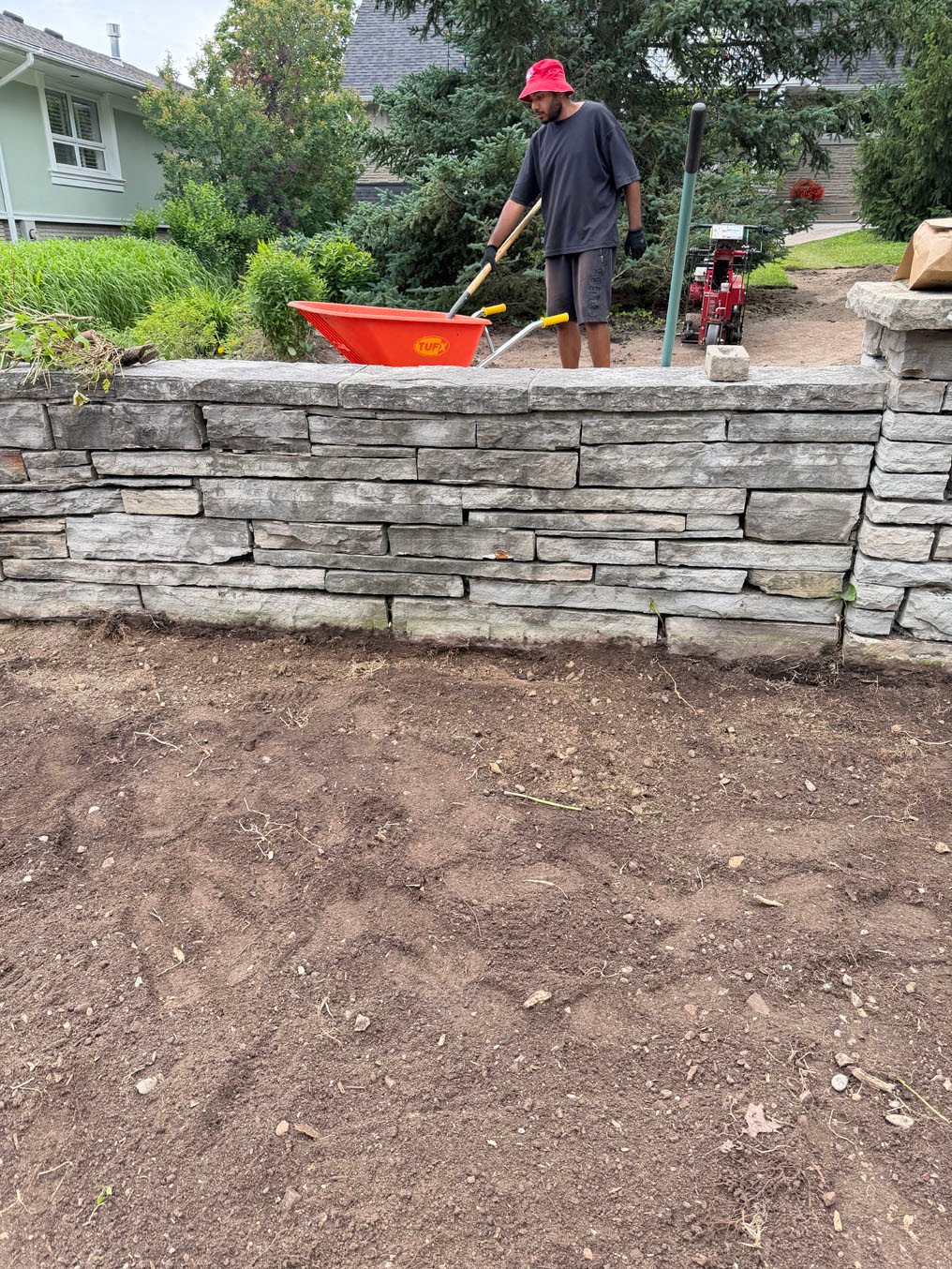 Sod Installation On Stanley Drive, Waterloo 7 Crew raking topsoil at the stone retaining wall with a wheelbarrow on Stanley Drive, Waterloo